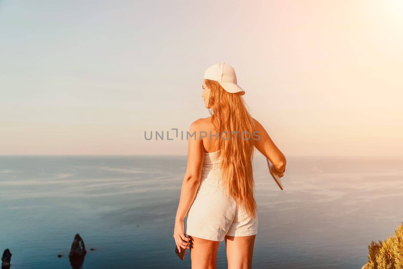 A female tourist stands by the sea wearing a white cap and T-shirt, looking happy and relaxed