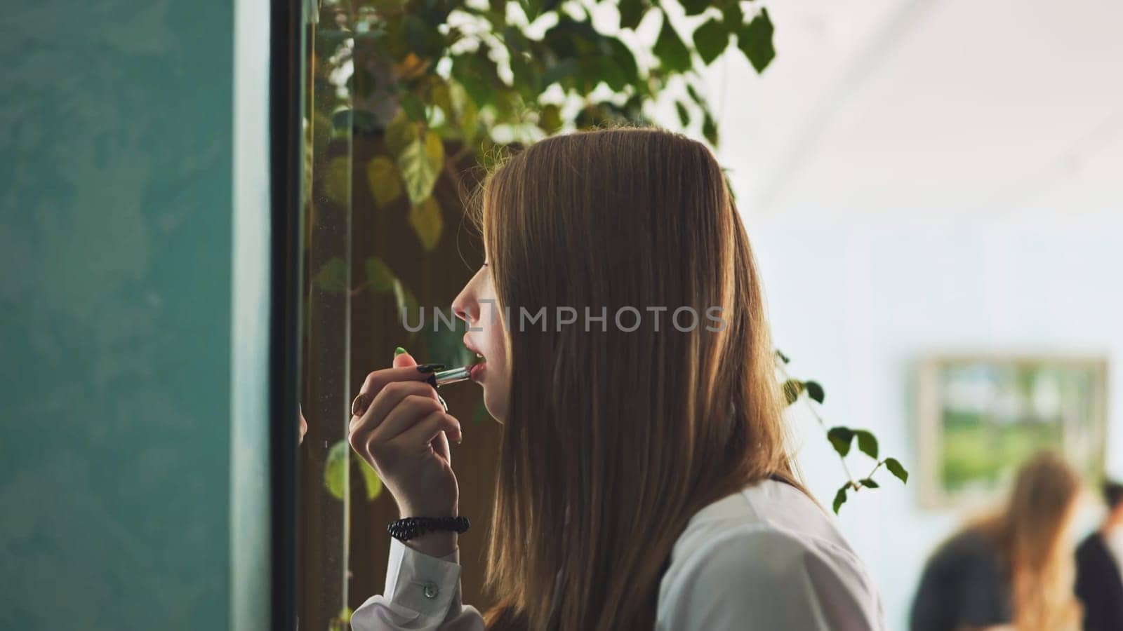 A schoolgirl paints her lips in front of the mirror