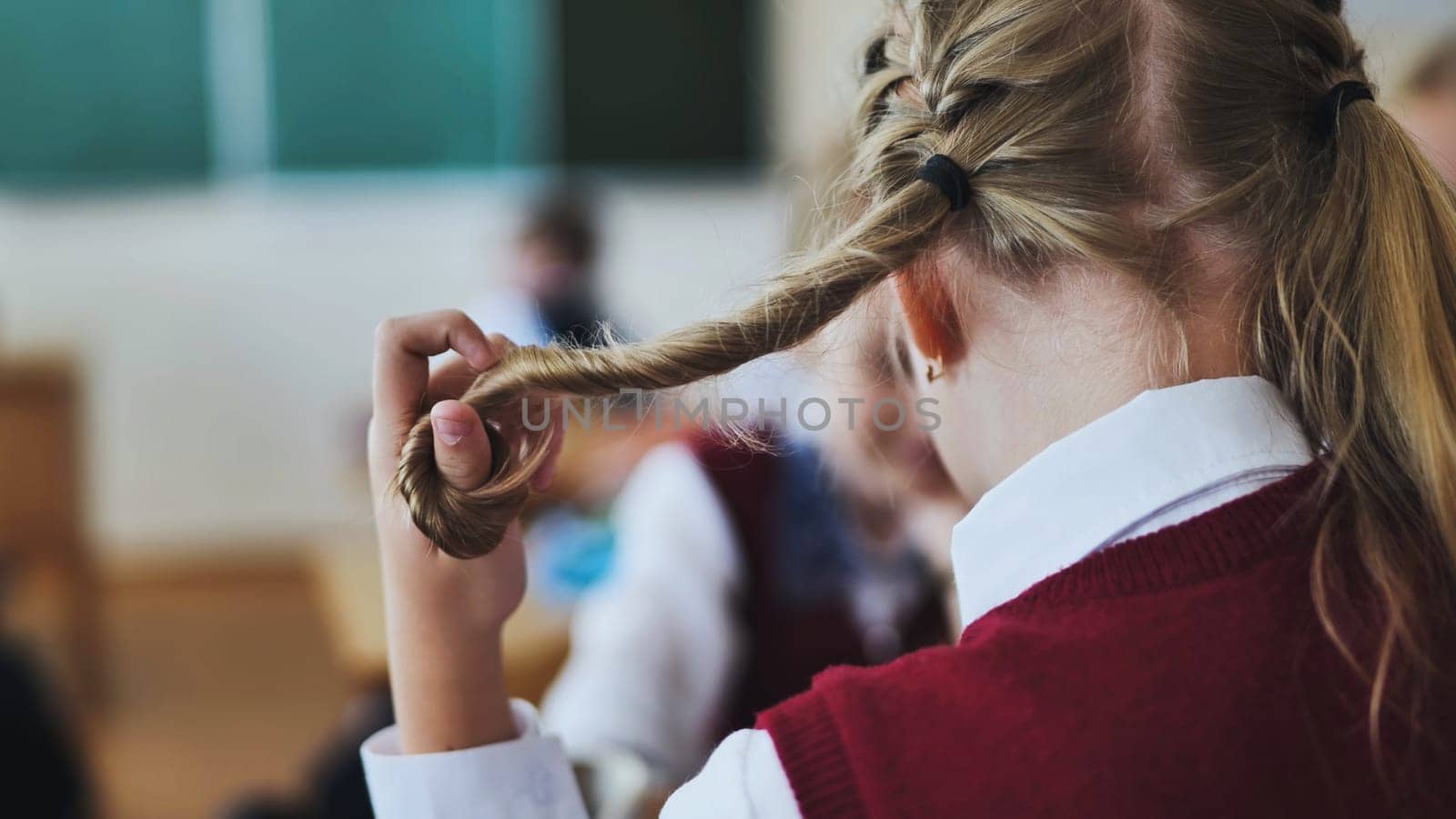 A girl touches a ponytail of her hair during class