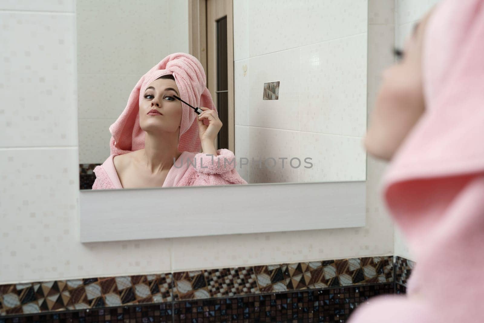 Sexy woman using mascara while looking at her reflection in mirror