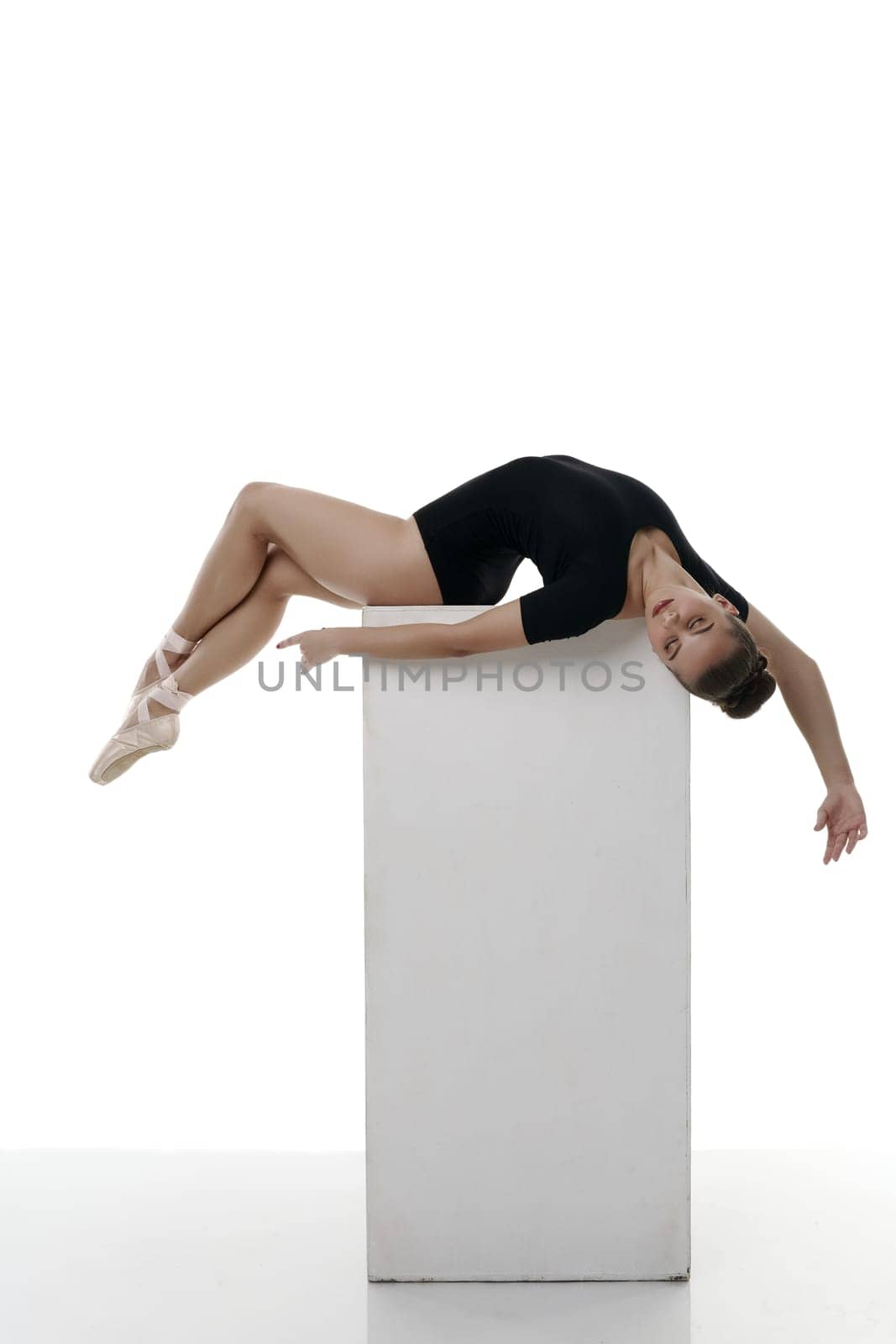 Studio photo of dreaming ballerina lying on cube