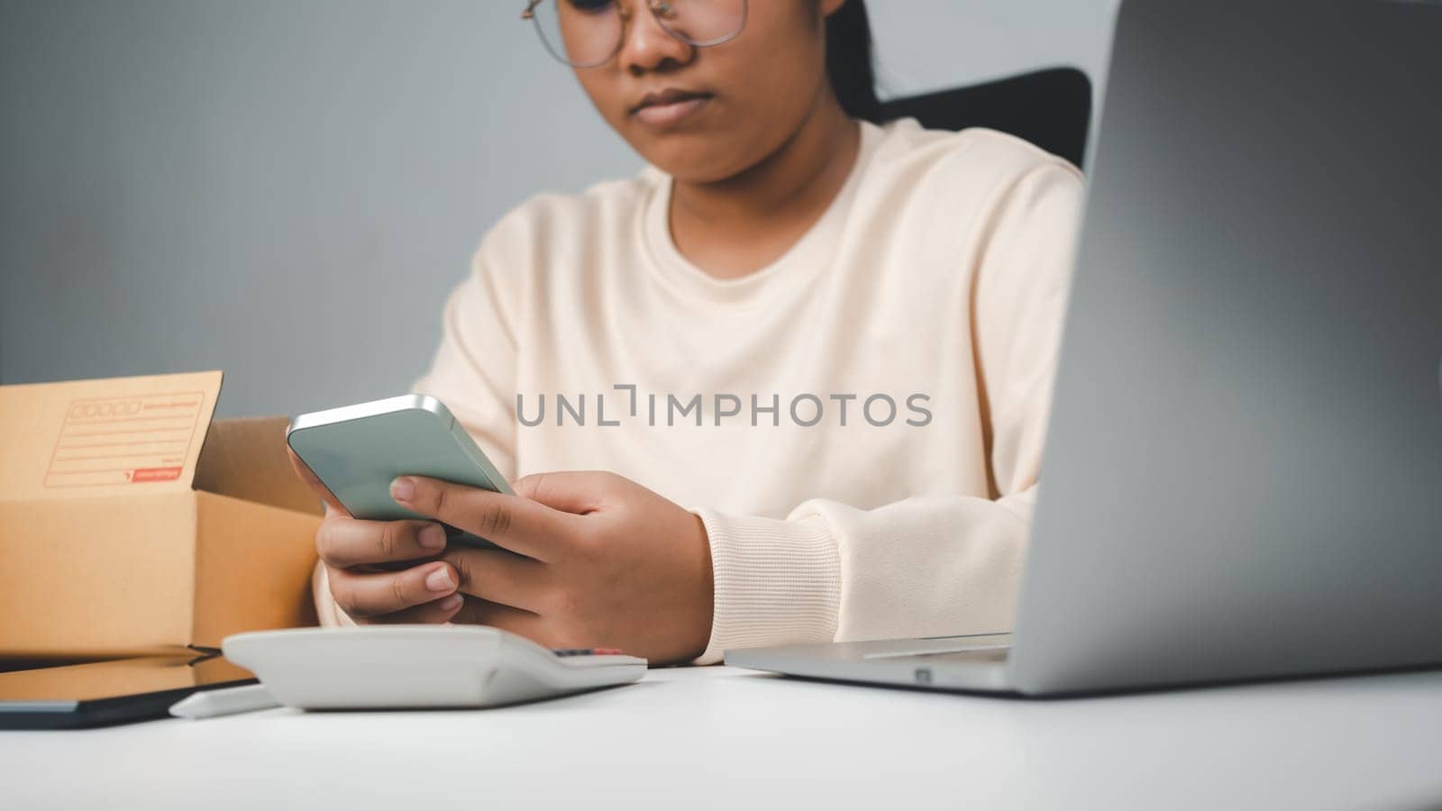 Woman runs an e-commerce business is checking orders from laptop, she owns an online store, she packs and ships through a private transport company. Online selling and online shopping concepts. by Unimages2527