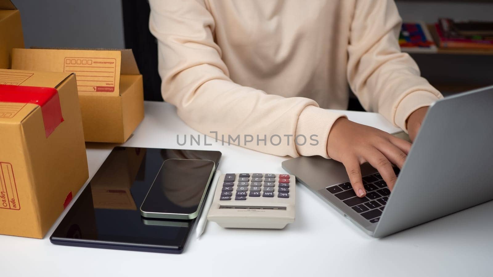 Woman runs an e-commerce business is checking orders from laptop, she owns an online store, she packs and ships through a private transport company. Online selling and online shopping concepts. by Unimages2527