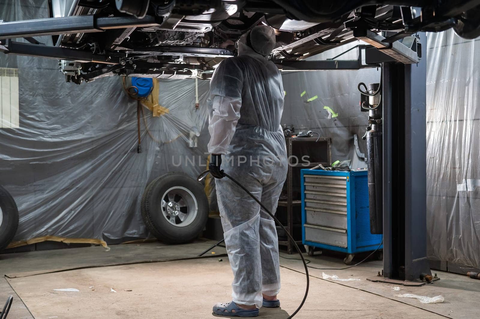 The master sprays an anti-corrosion compound on the bottom of the car
