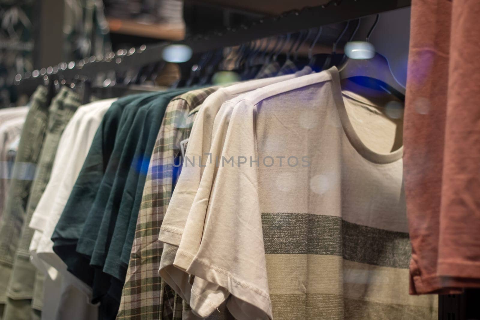 A row of Fashion design shirts, including Denim and Sportswear in Electric blue, are hanging on Clothes hangers in a Retail store