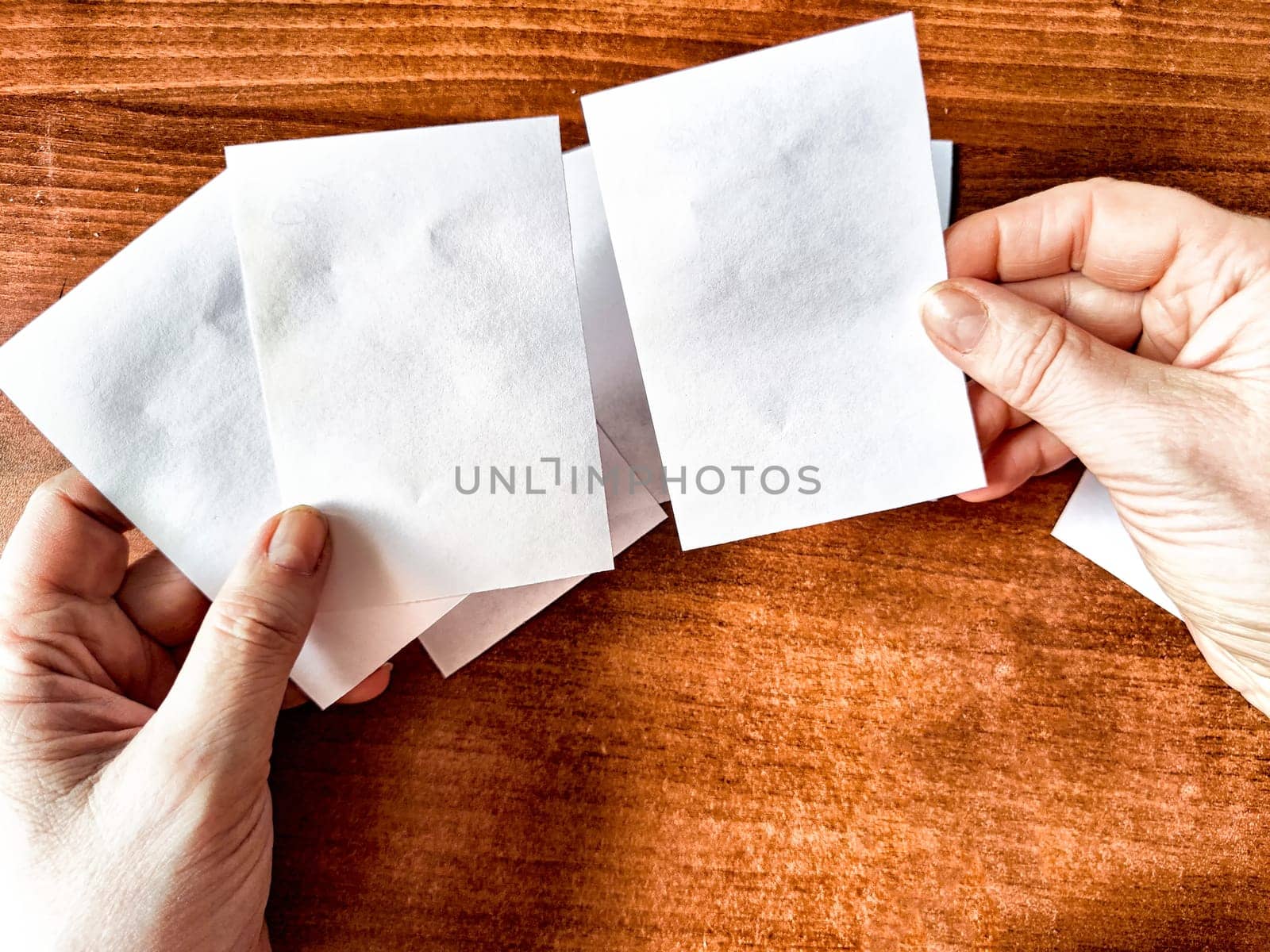 Woman Holding Small White Papers Over a Wooden Surface. Hands presenting several small white papers by keleny