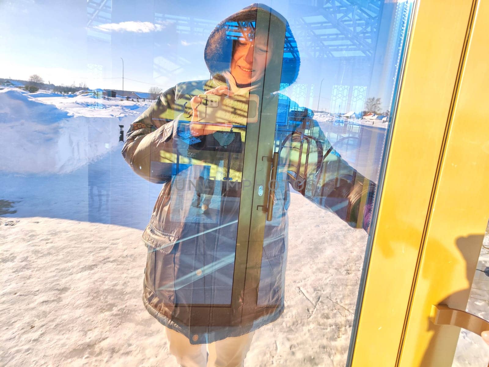 Woman Capturing Her Reflection in Snowy Doorway. A woman takes a reflective selfie amidst winter scenery