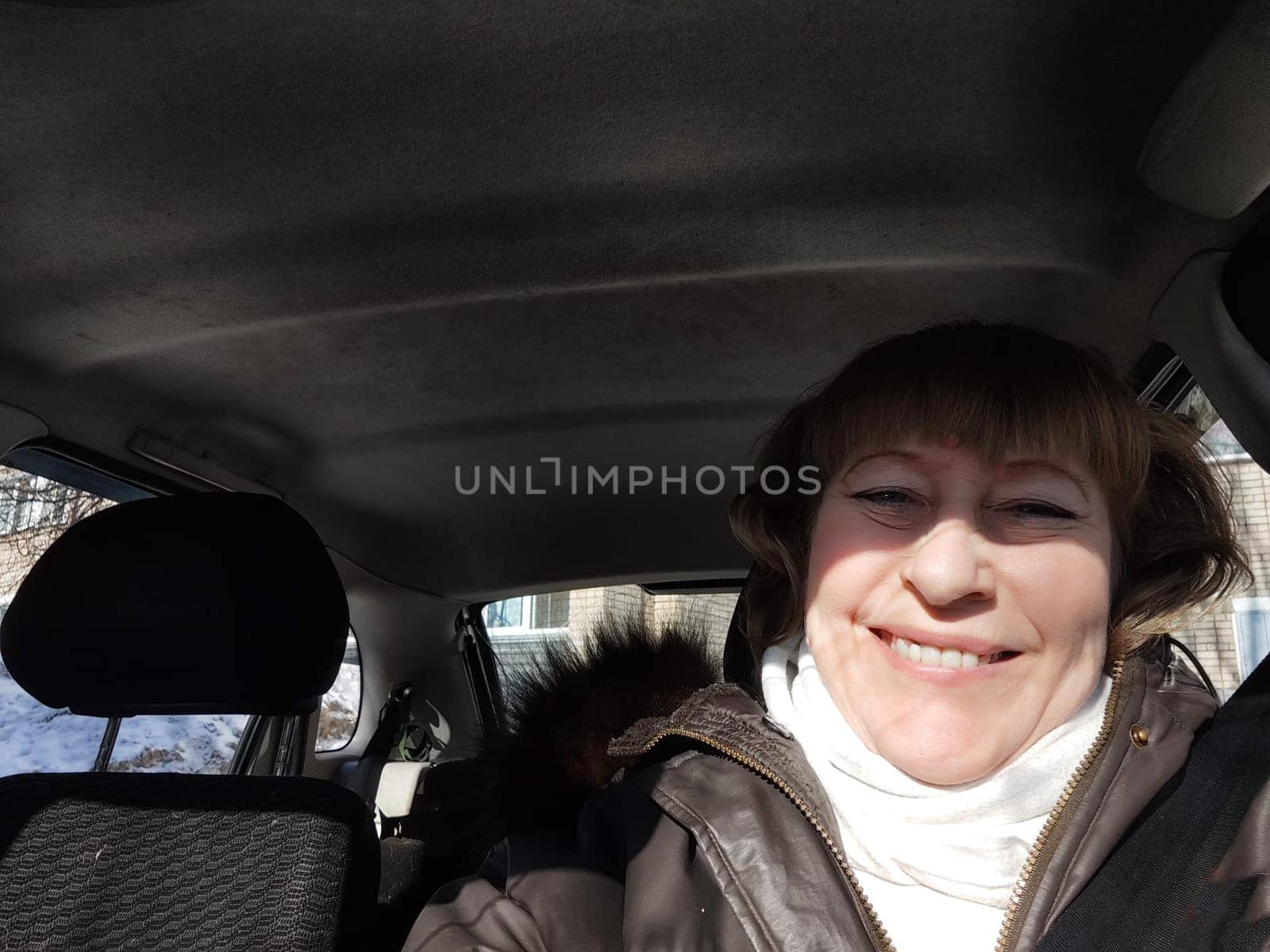 Middle aged woman in a car taking a selfie while enjoying a drive. Female mature driver posing inside car. Funny happy tourist girl in alone travel