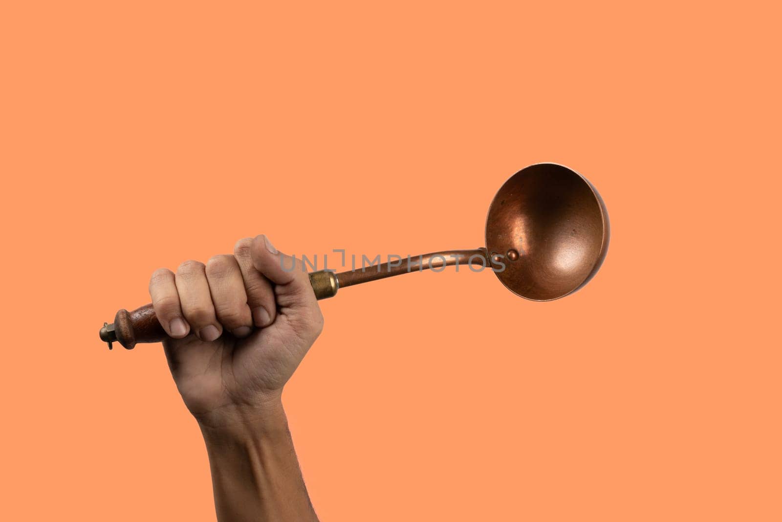 Black male hand holding a brass vintage kitchen ladle isolated orange background. High quality photo