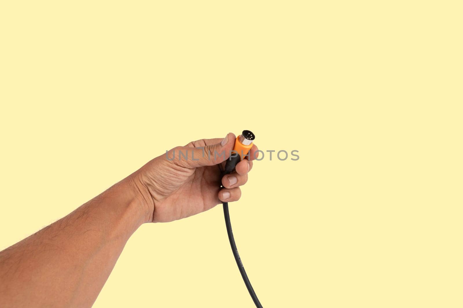 Black male hand holding a MIDI audio cable isolated light yellow background. High quality photo