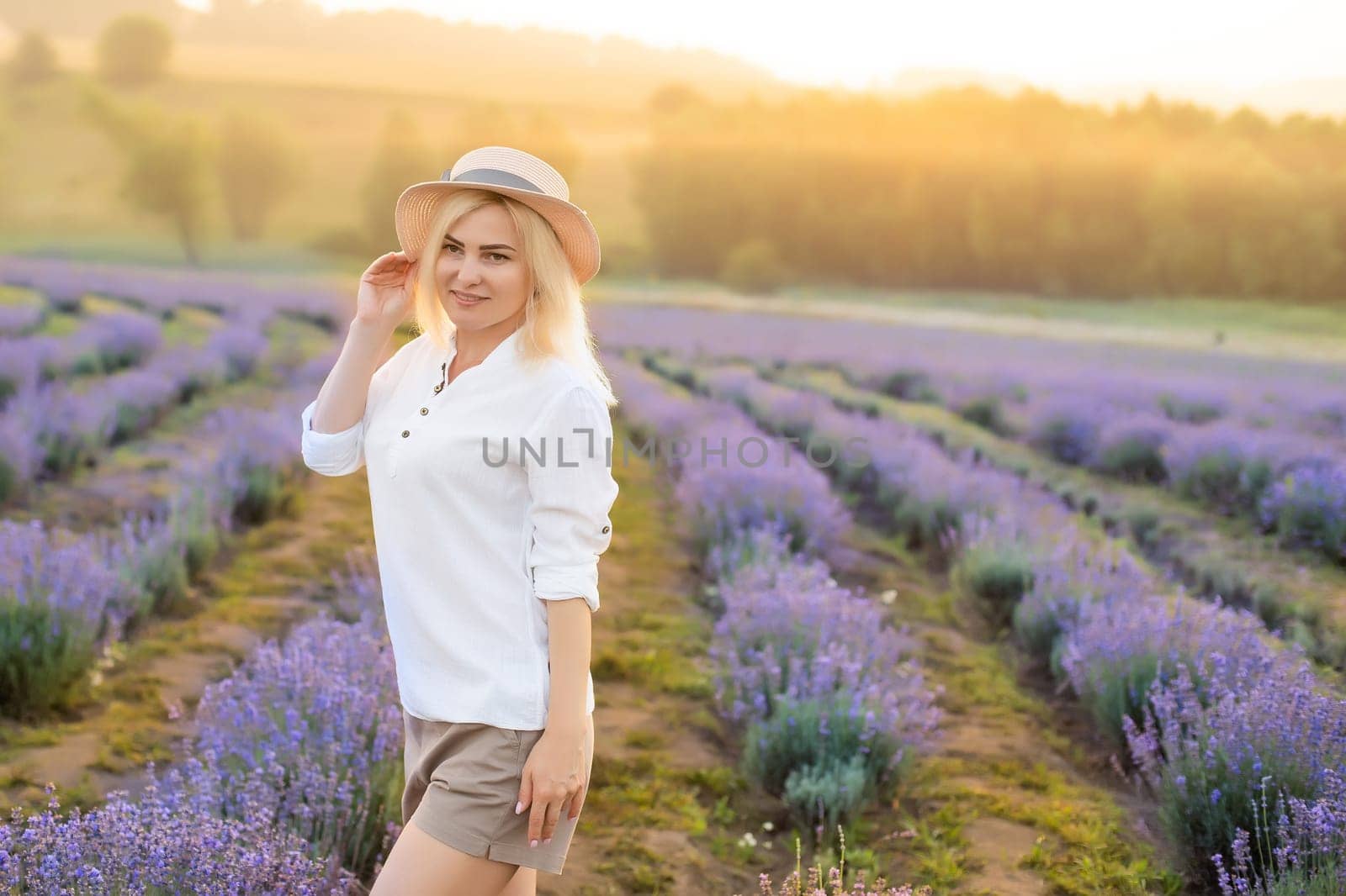 Young blond woman traveller wearing straw hat in lavender field surrounded with lavender flowers. by Andelov13