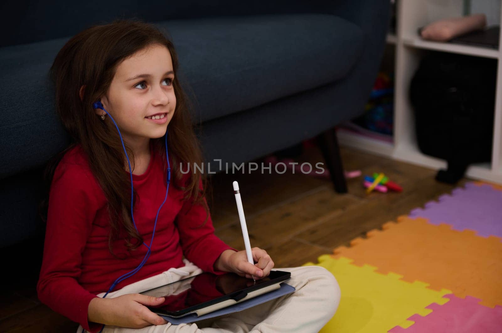 Adorable little child girl holding digital tablet and white stylus, learning online, doing homework, drawing pictures, watching cartoons or listening to online webinar class. Kids and technology by artgf