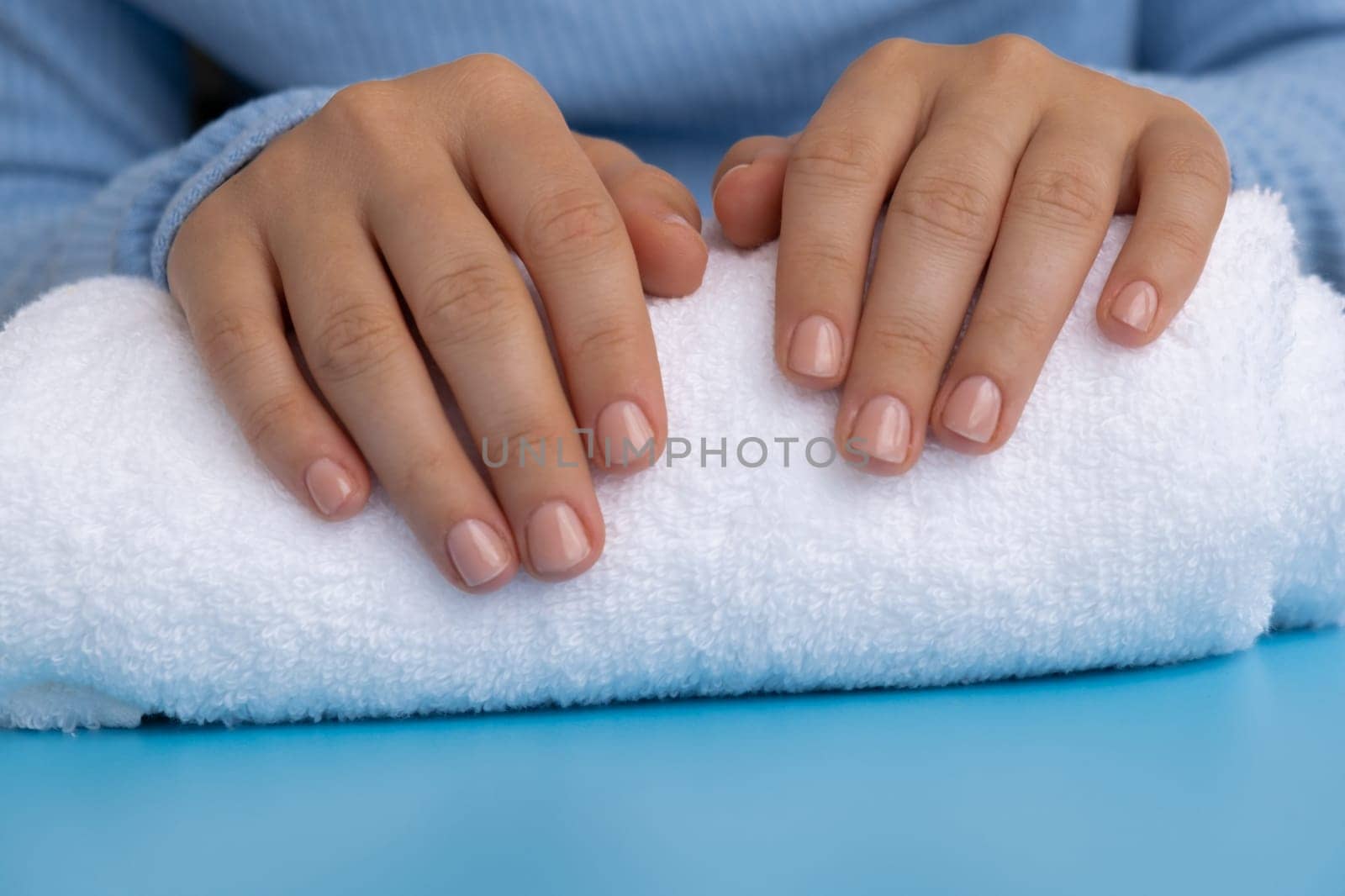 Woman manicured hands, stylish beige nails. Closeup of manicured nails of female hand in blue sweater in blue background. Winter or autumn style of nail design concept by anna_stasiia