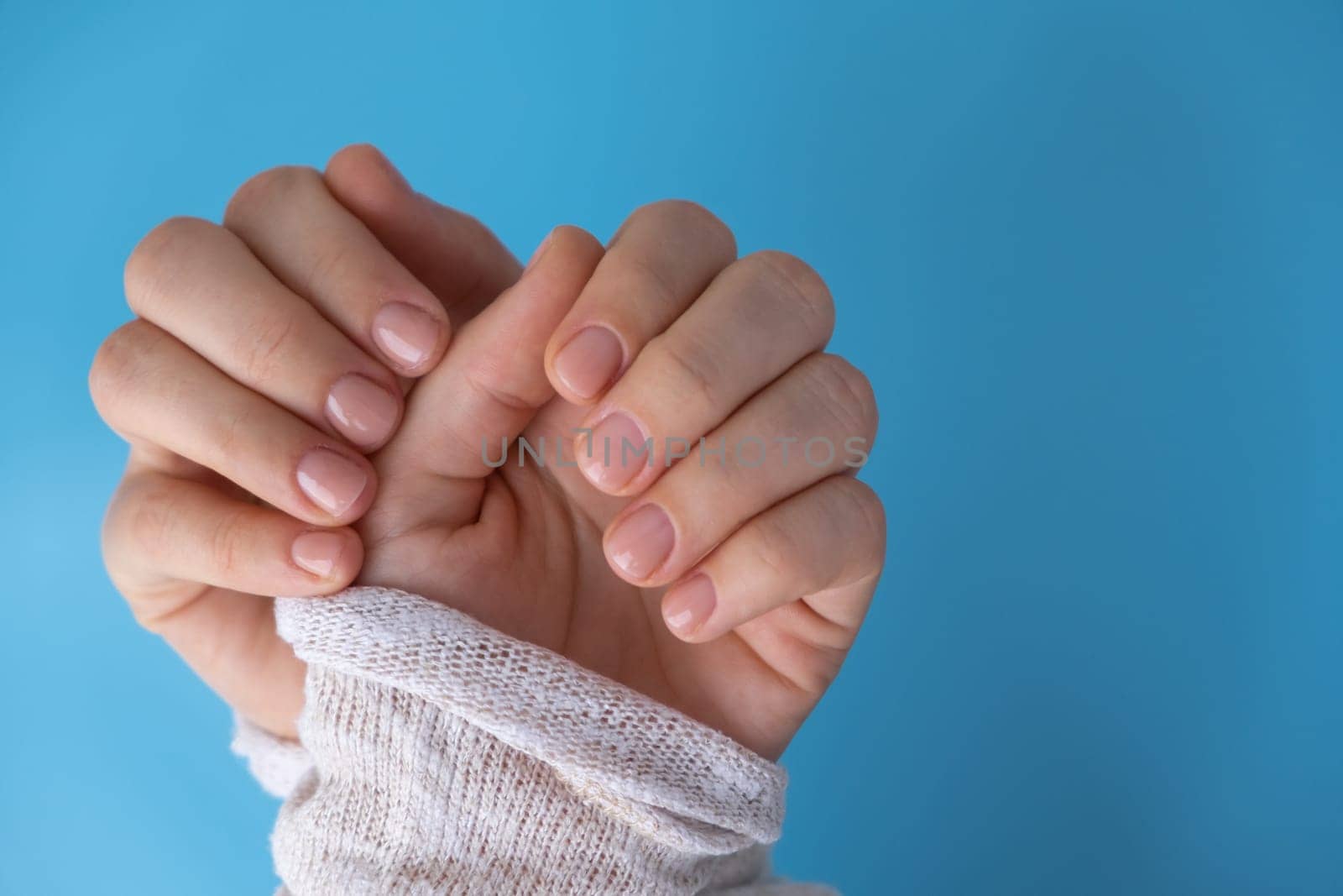 Pastel softness manicured nails on blue background. Woman showing her new manicure in colors of pastel palette. Simplicity decor fresh spring vibes earth-colored neutral tones by anna_stasiia