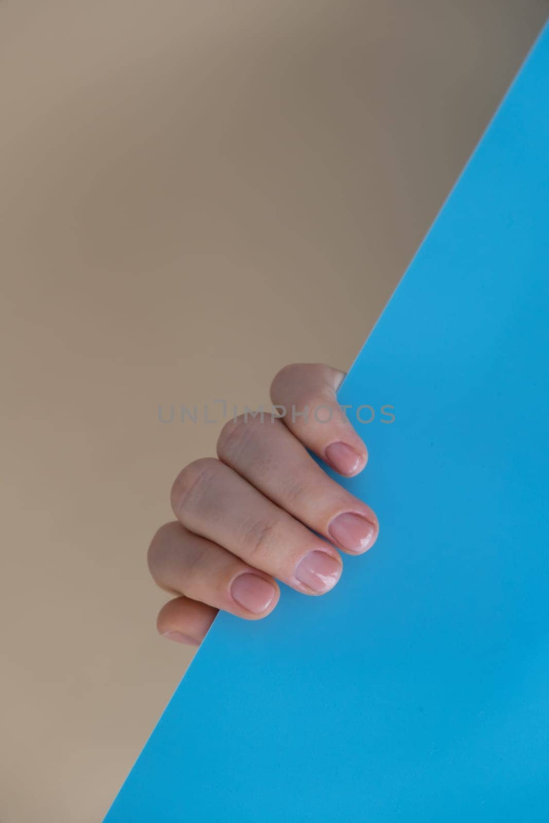 Stylish nude beige female nails on blue beige background. Modern trendy stylish Beautiful manicure. Cute pastel nail minimalistic design concept of beauty treatment. Gel nails. Skin care. Beautician