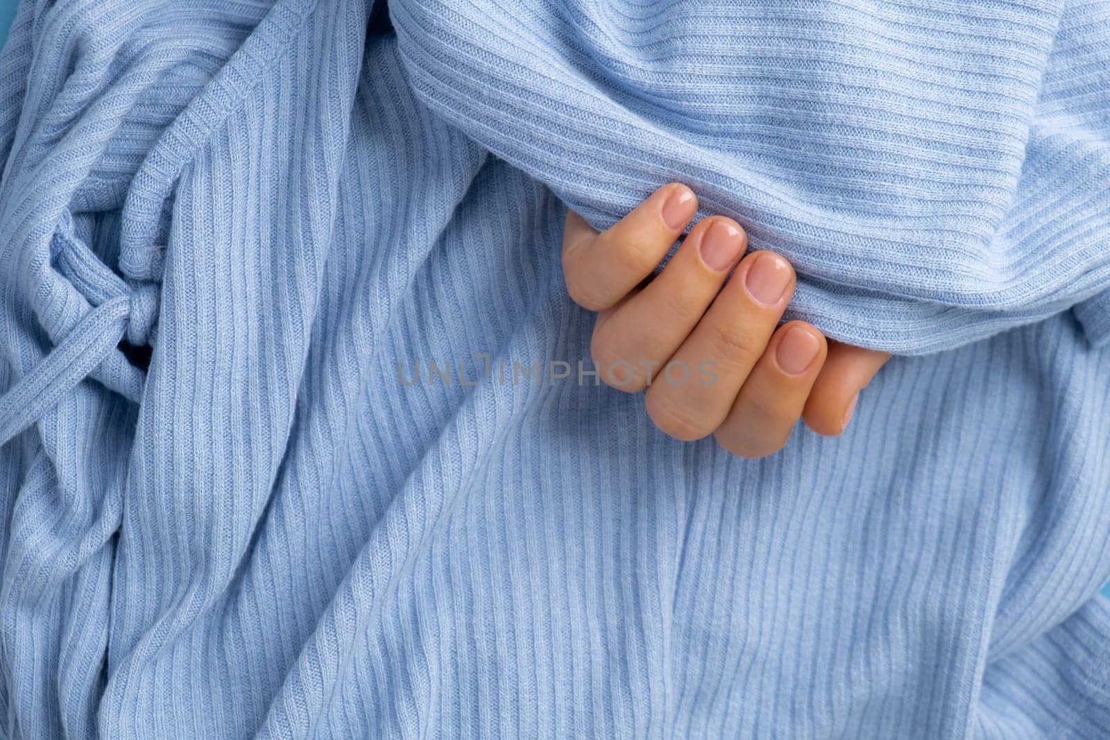 Woman manicured hands, stylish beige nails. Closeup of manicured nails of female hand in blue sweater in blue background. Winter or autumn style of nail design concept. Beauty treatment.