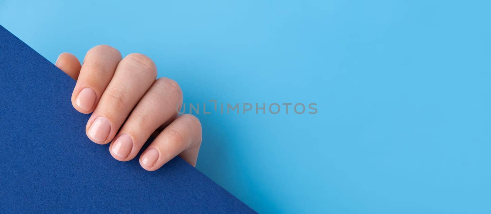 Pastel softness manicured nails on blue background. Mock up template copy space Woman showing her new manicure in colors of pastel palette. Simplicity decor fresh spring vibes earth-colored neutral tones design