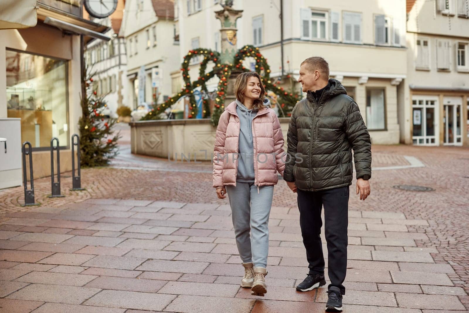 Loving couple of tourists walking around old town. Couple of lovers leisurely stroll in the cool autumn morning on the streets of a BIETIGHEIM-BISSINGEN (Germany). The guy holds his wife. Vacation, Winter, holiday. Romantic Stroll through Historic German Charm. Couple Walking in Europe's Old Town by Andrii_Ko