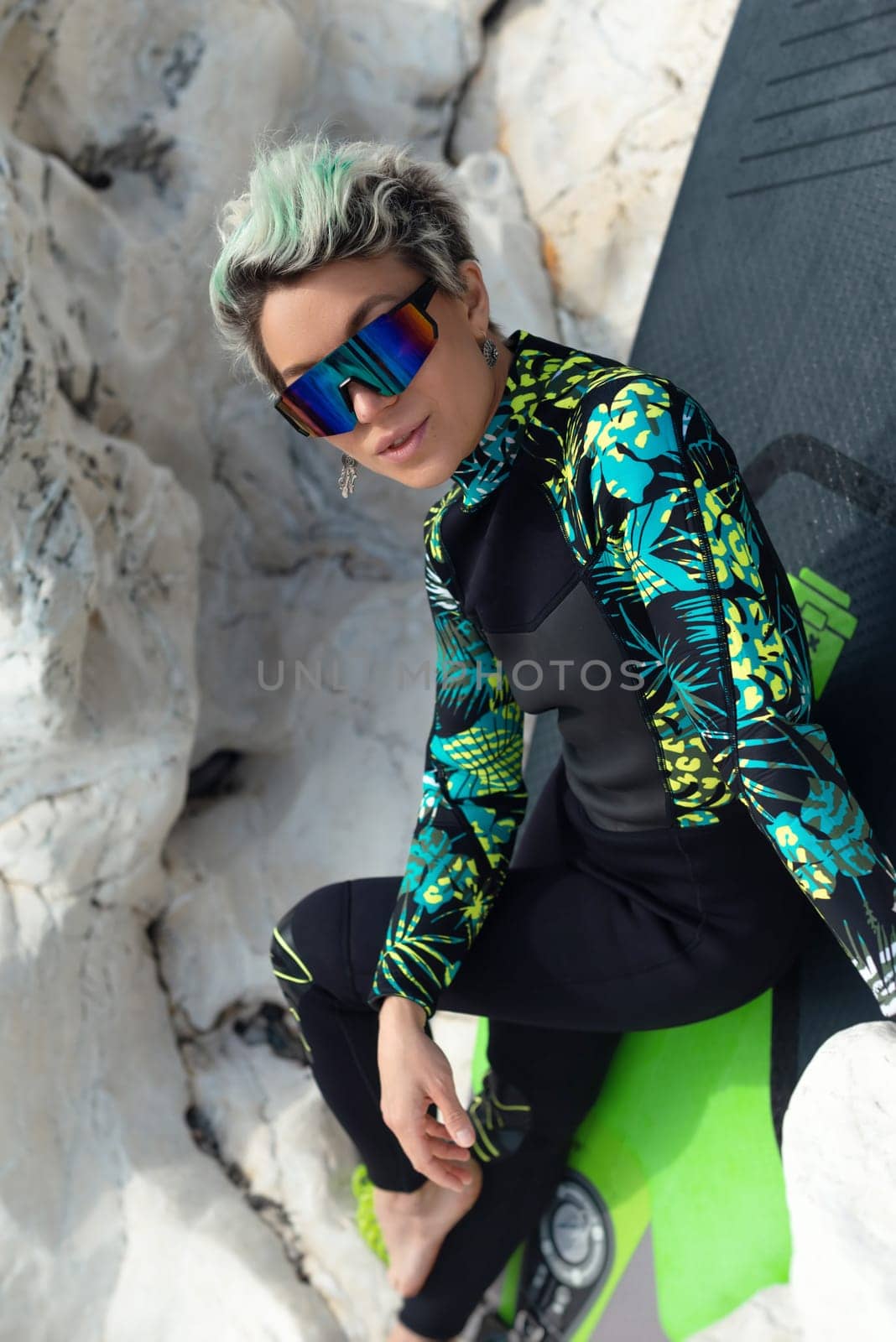 A beautiful sup surfer girl in a wetsuit on the ocean shore against a beautiful blue sky poses sexually with a paddle by Rotozey