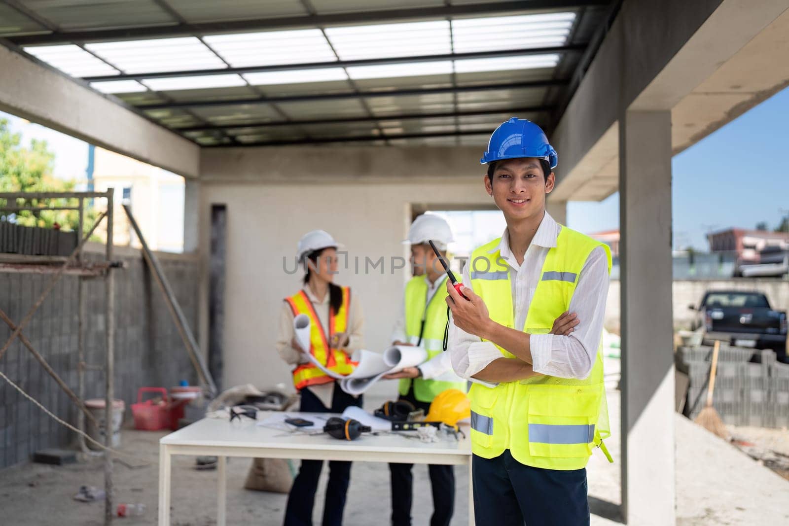 electrical engineer stand with walkie-talkie in construction building and engineer colleagues are working in the background.