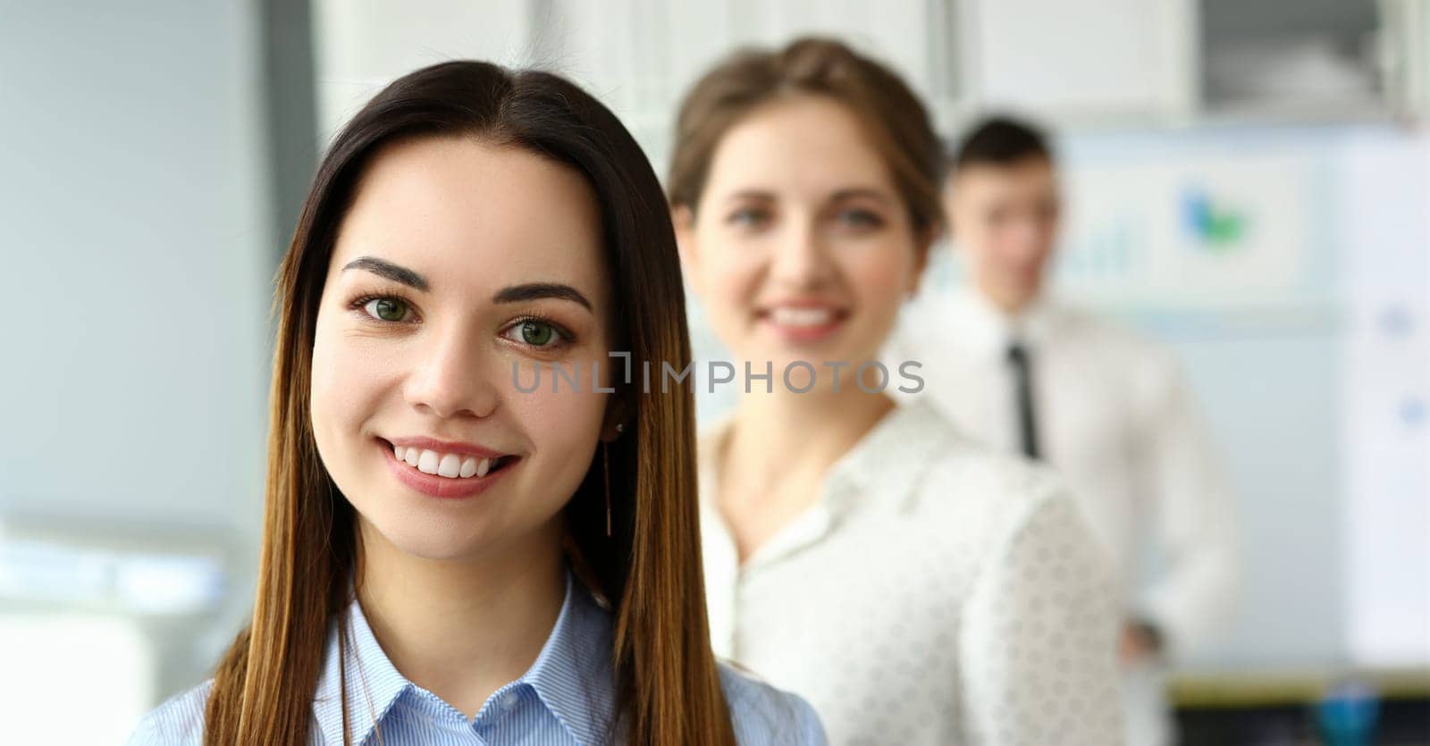 Portrait of smart woman standing in big modern office working with great friendly collective and looking at camera with joy and calmness. Company meeting concept