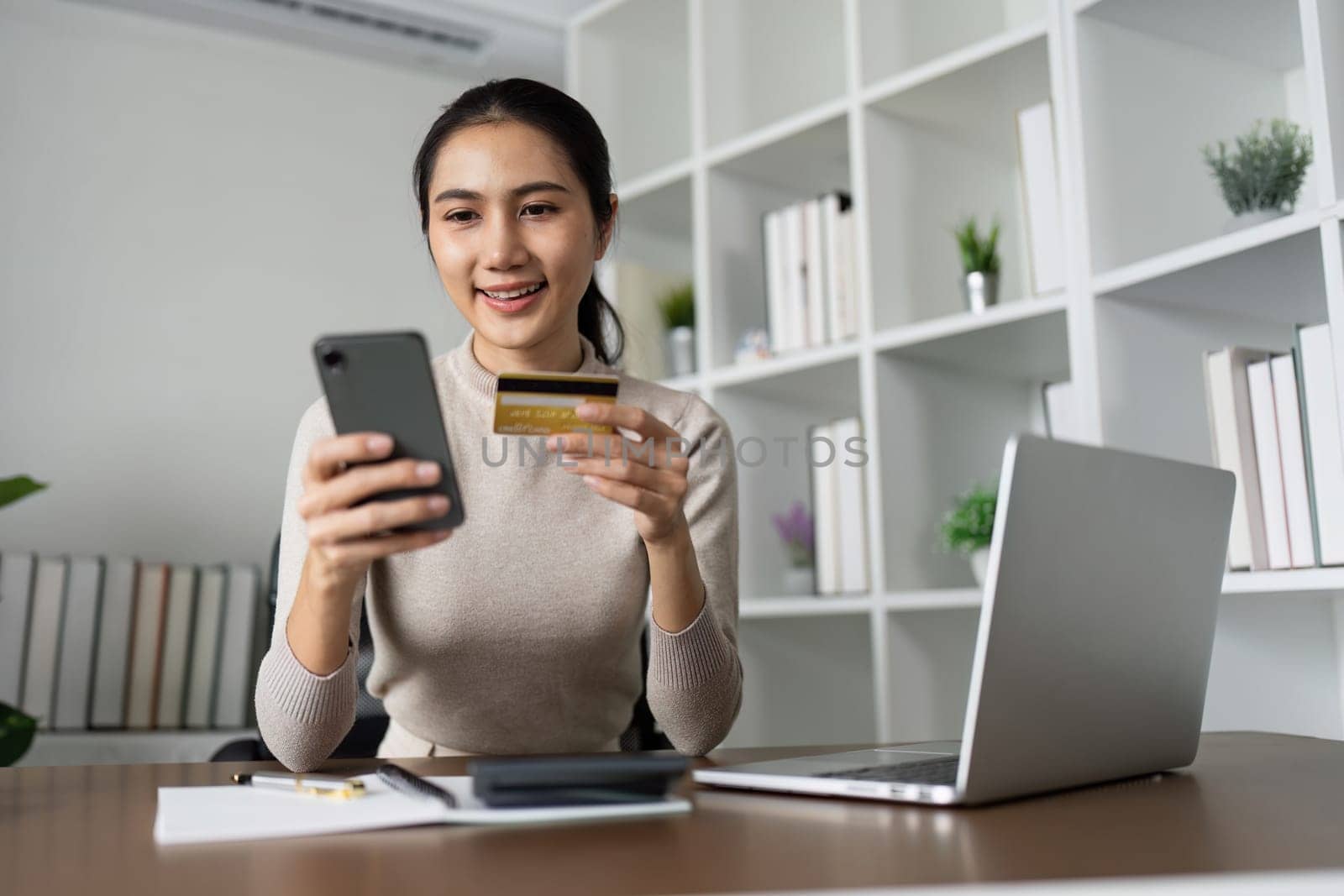 Woman using laptop computer and mobile phone holding credit card for shopping online.