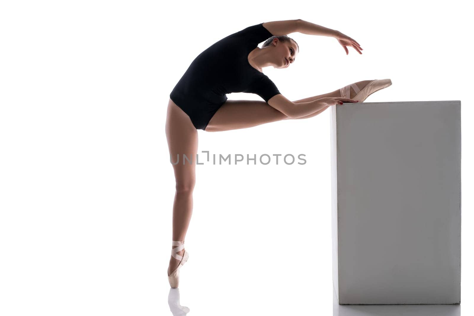 Studio image of ballerina putting her leg on cube while warming up