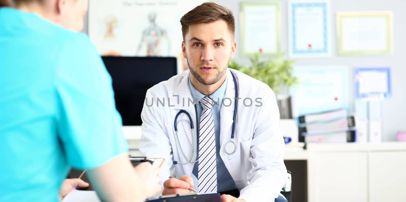 Portrait of worried man sitting in clinic office and having disturbing conversation with colleague. Physician in classy shirt and tie look at camera with desperation. Medical treatment concept