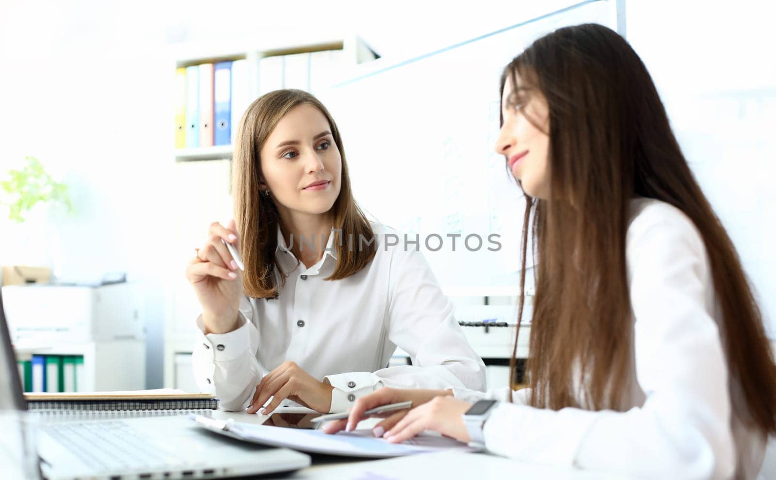 Portrait of beautiful businesswoman sitting at modern workplace and talking with smart woman colleague about important business project. Accounting office concept