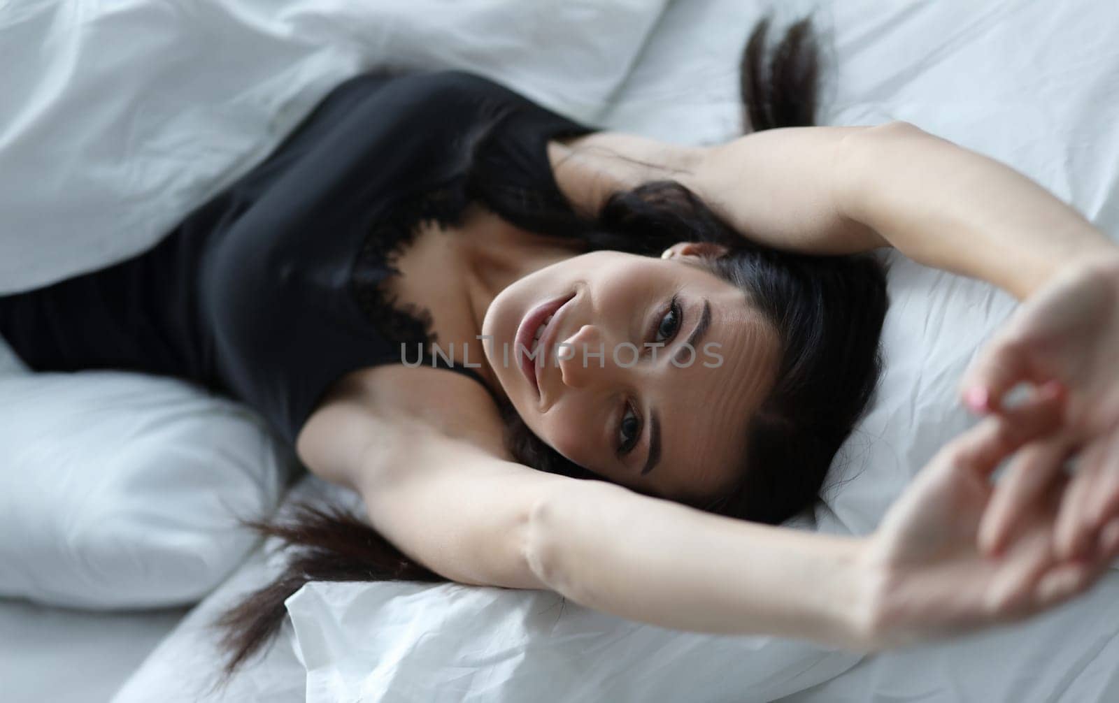 Woman in black peignoir stretches early in morning in bed. Good day concept