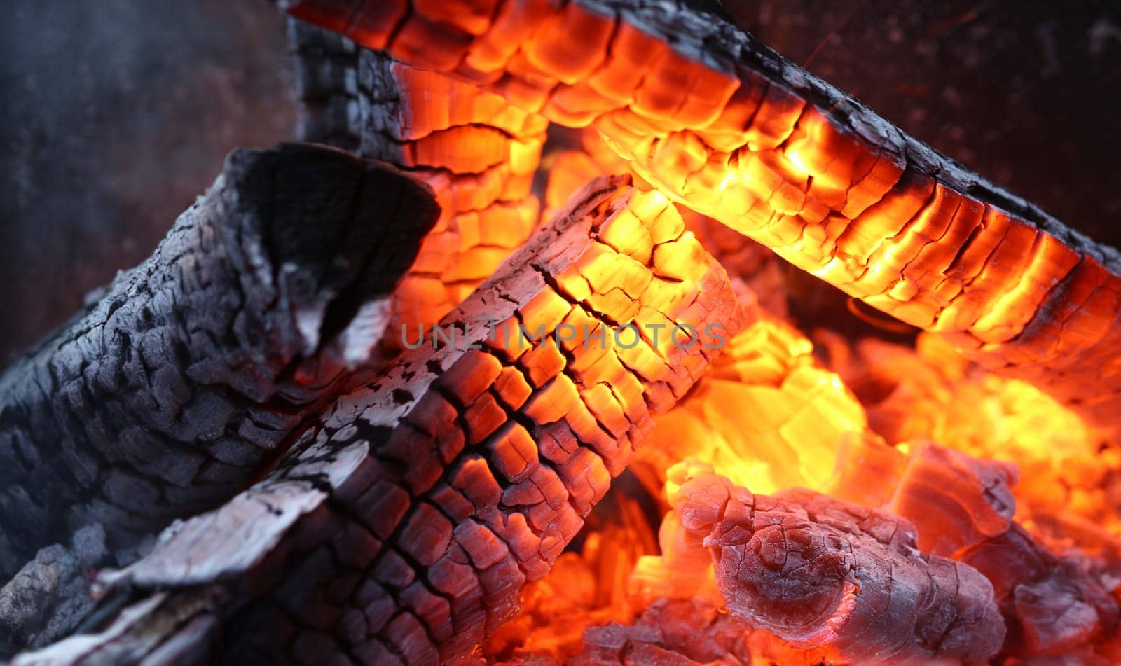 Close-up of burning log in bonfire. Large orange flame from fire with woods. Light and ash from wood in balefire. Amazing campfire with dark view outdoor