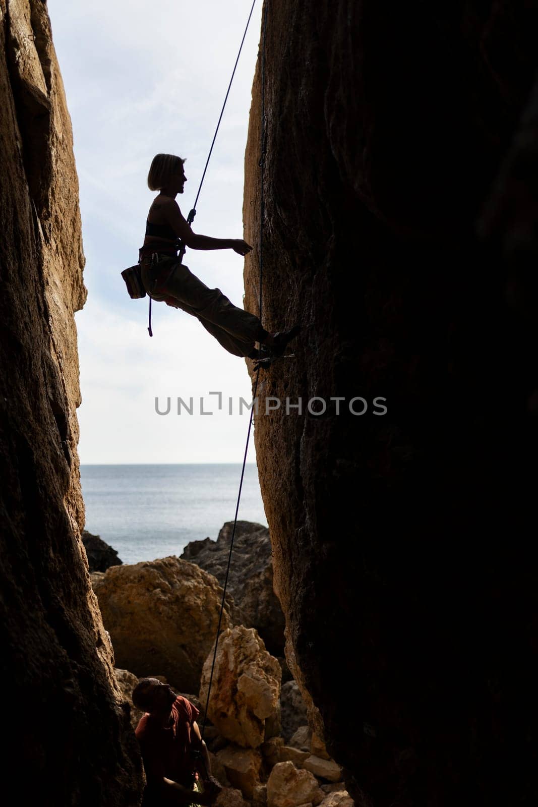 A woman is climbing a rock wall with a rope by Studia72