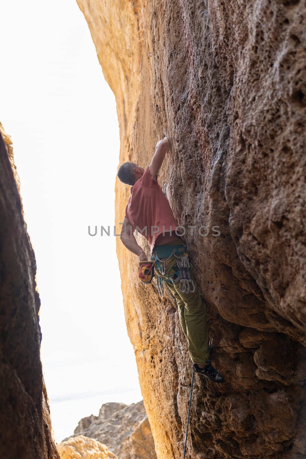 A man is climbing a rock wall with a yellow rope. The sun is shining on the wall, creating a warm and inviting atmosphere. The man is focused on his climb, and the image conveys a sense of adventure