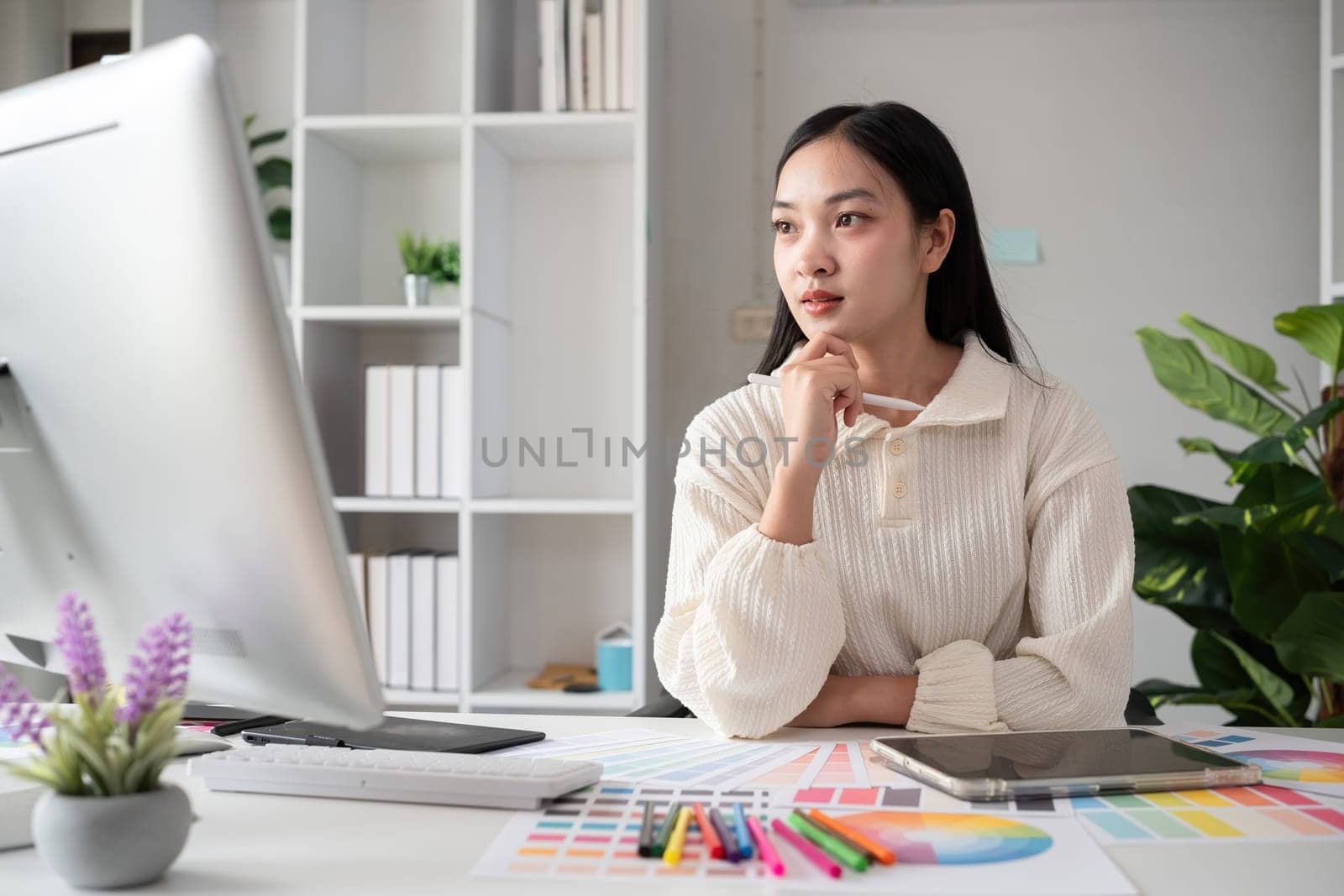 Female designer working in graphic design on computer Sit and choose colors and work intently in your office. by wichayada