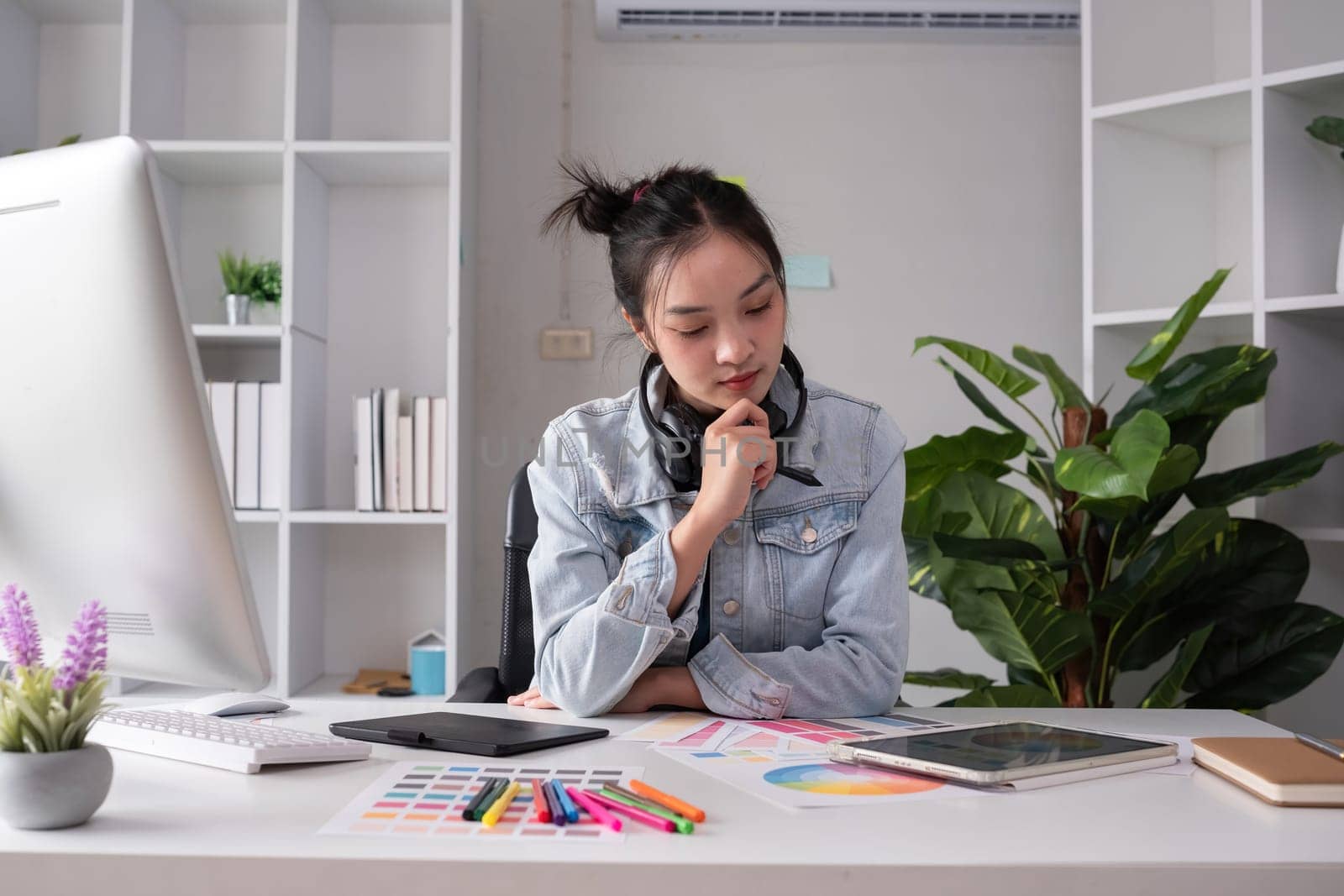 Female designer wearing headphones listening to music while doing graphic design work Choose colors for working with the computer at the table. by wichayada