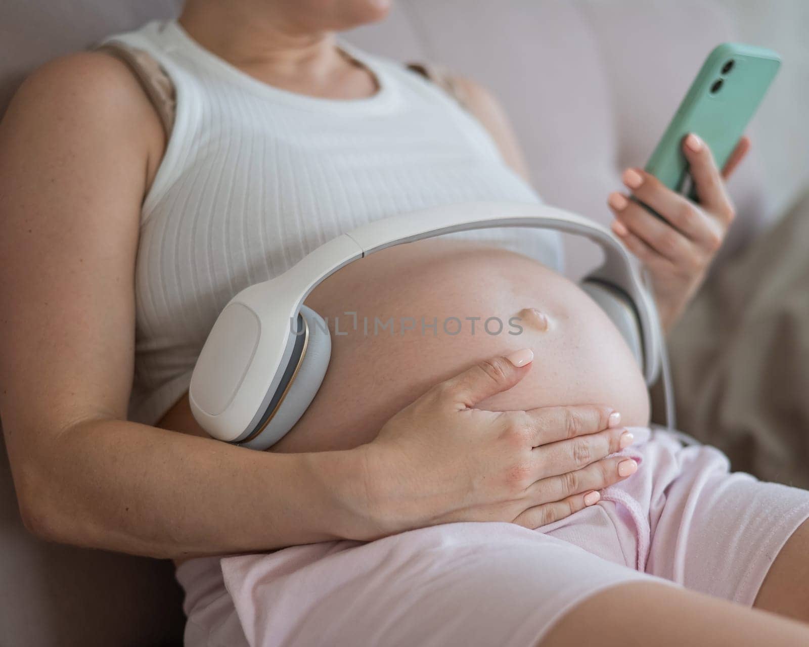 A pregnant woman turns on music for her child on a smartphone. Headphones on the tummy. by mrwed54