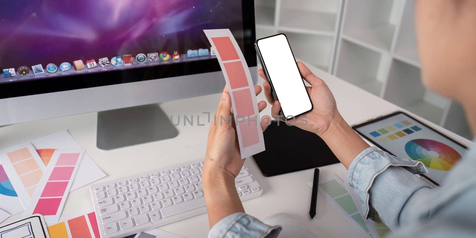 Woman hands holding a smartphone white screen mockup over modern graphic designer office desk by nateemee