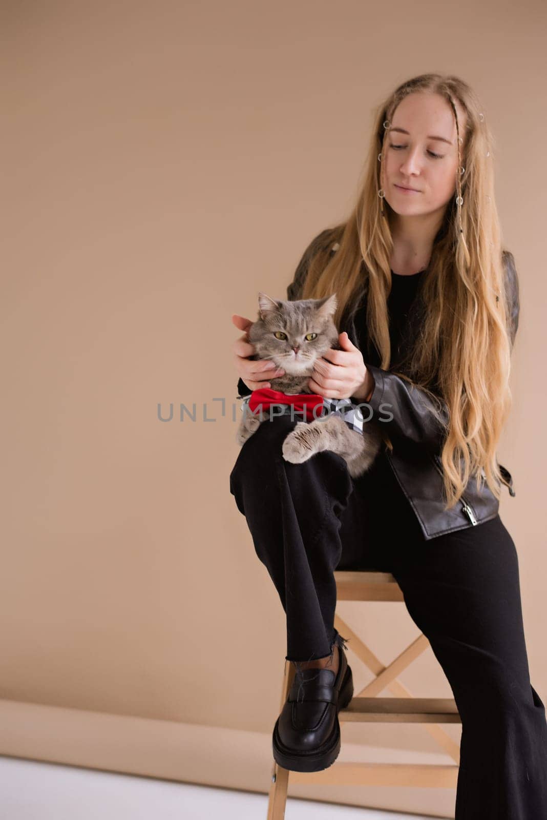 A woman natural blonde long hair smiling in a black clothes, sitting on photo studio. girl with pet scottish straight cat. portrait , vertical,