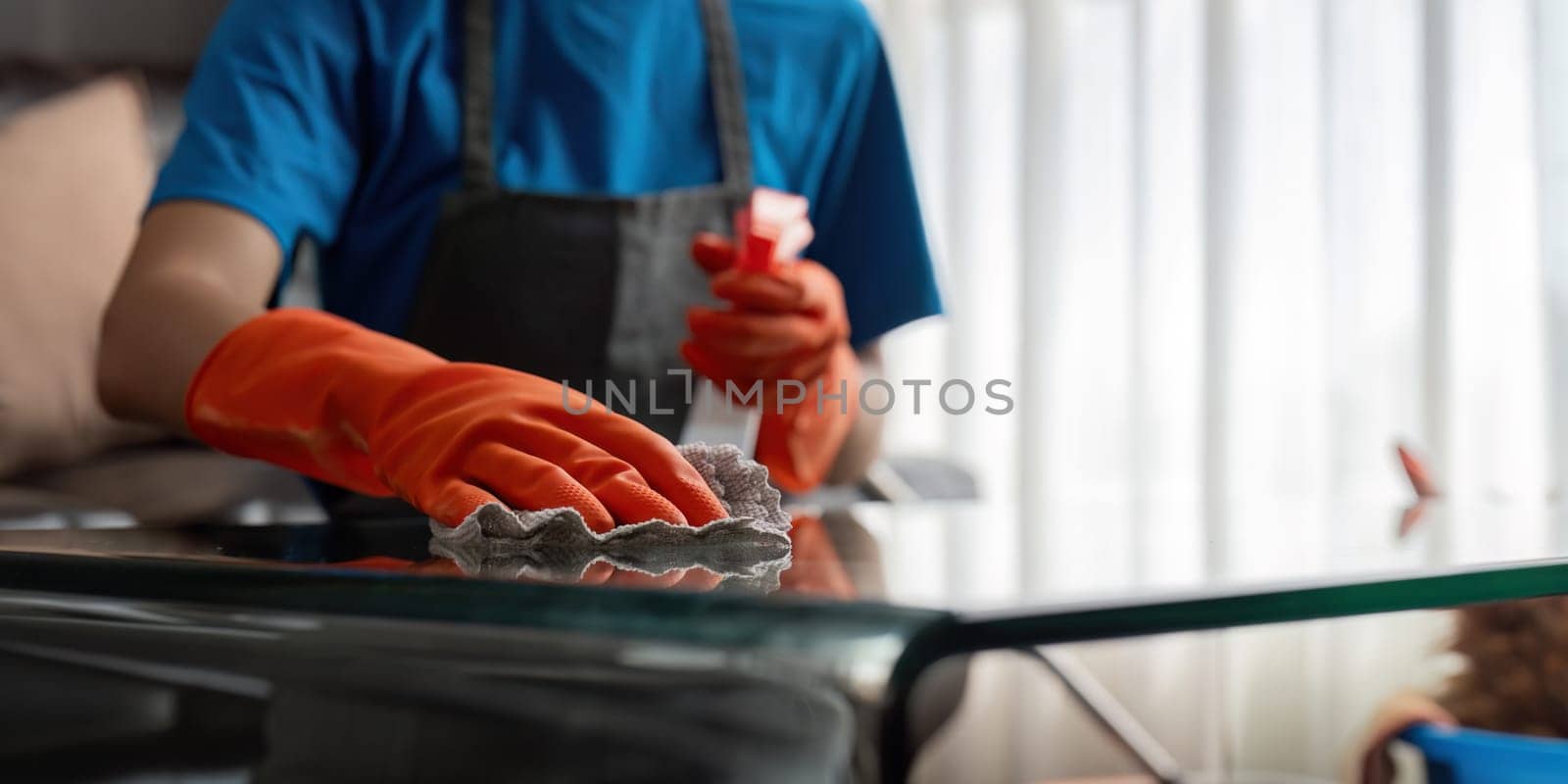 Asian woman cleaning the glass table in the apartment. Cleaning staff maintain cleanliness in with towel and spray detergent.