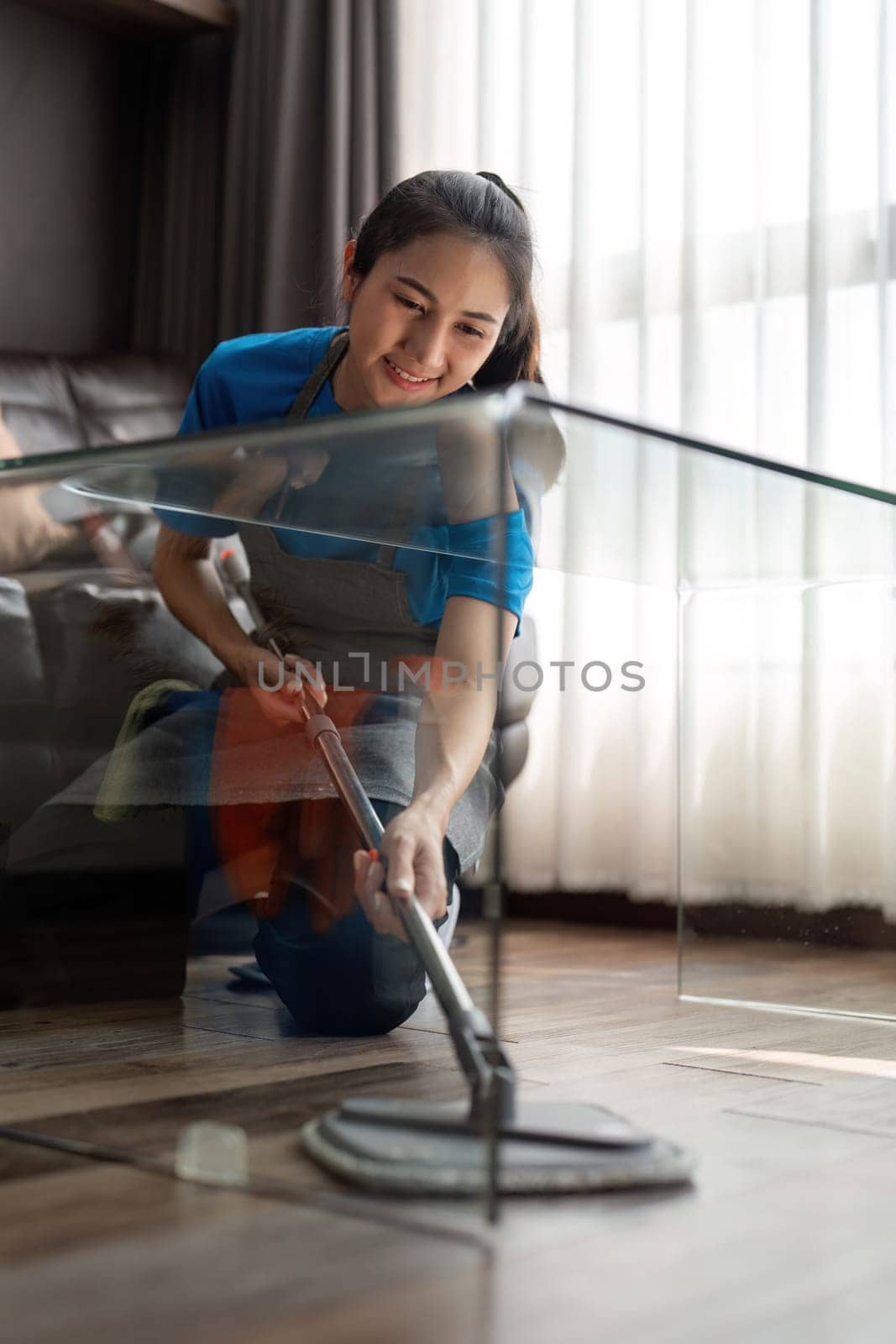 Asian cleaning service woman worker cleaning in living room at home. Beautiful young girl housekeeper cleaner wear apron and wipe messy dirty floor for housekeeping housework in house.