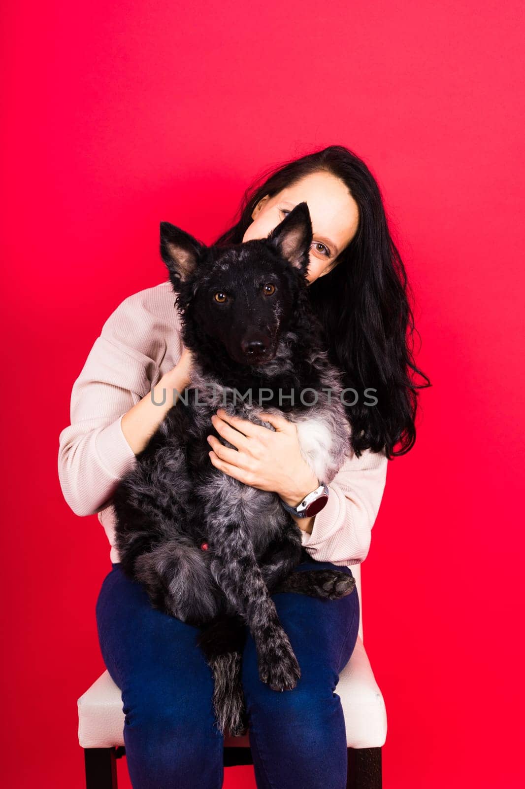 Happy brunette lady in a casual wear hugging mudi pet dog, studio background.