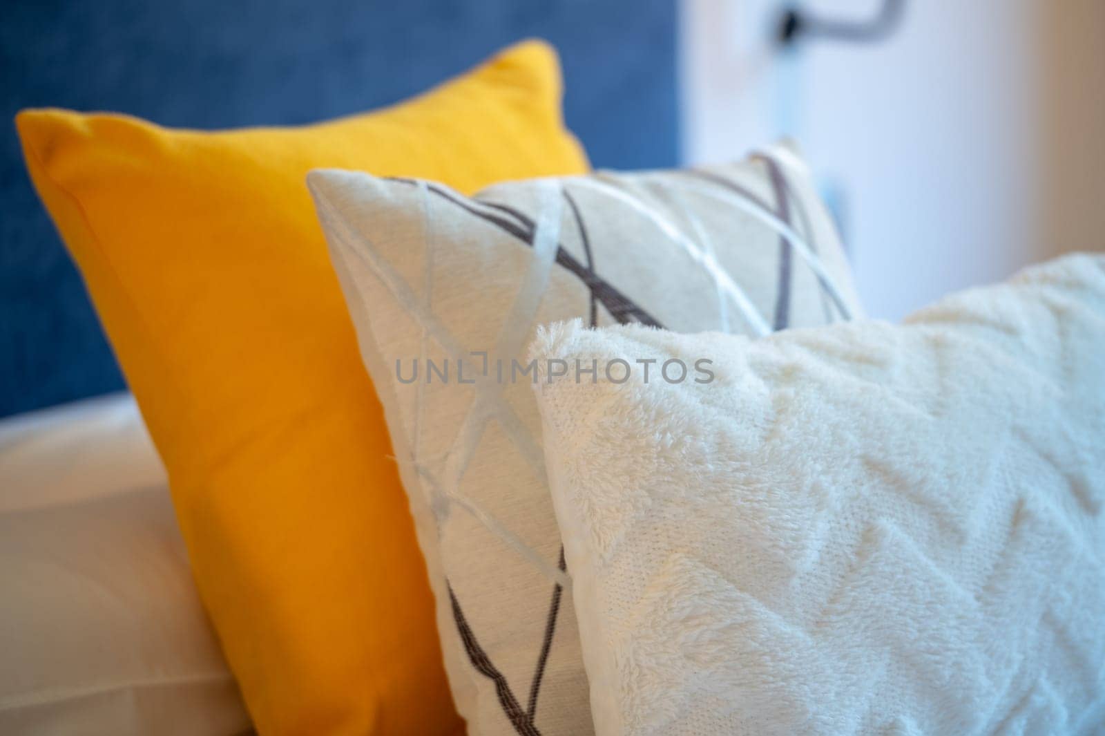 Colorful cushions on bed in illuminated room. by martinscphoto