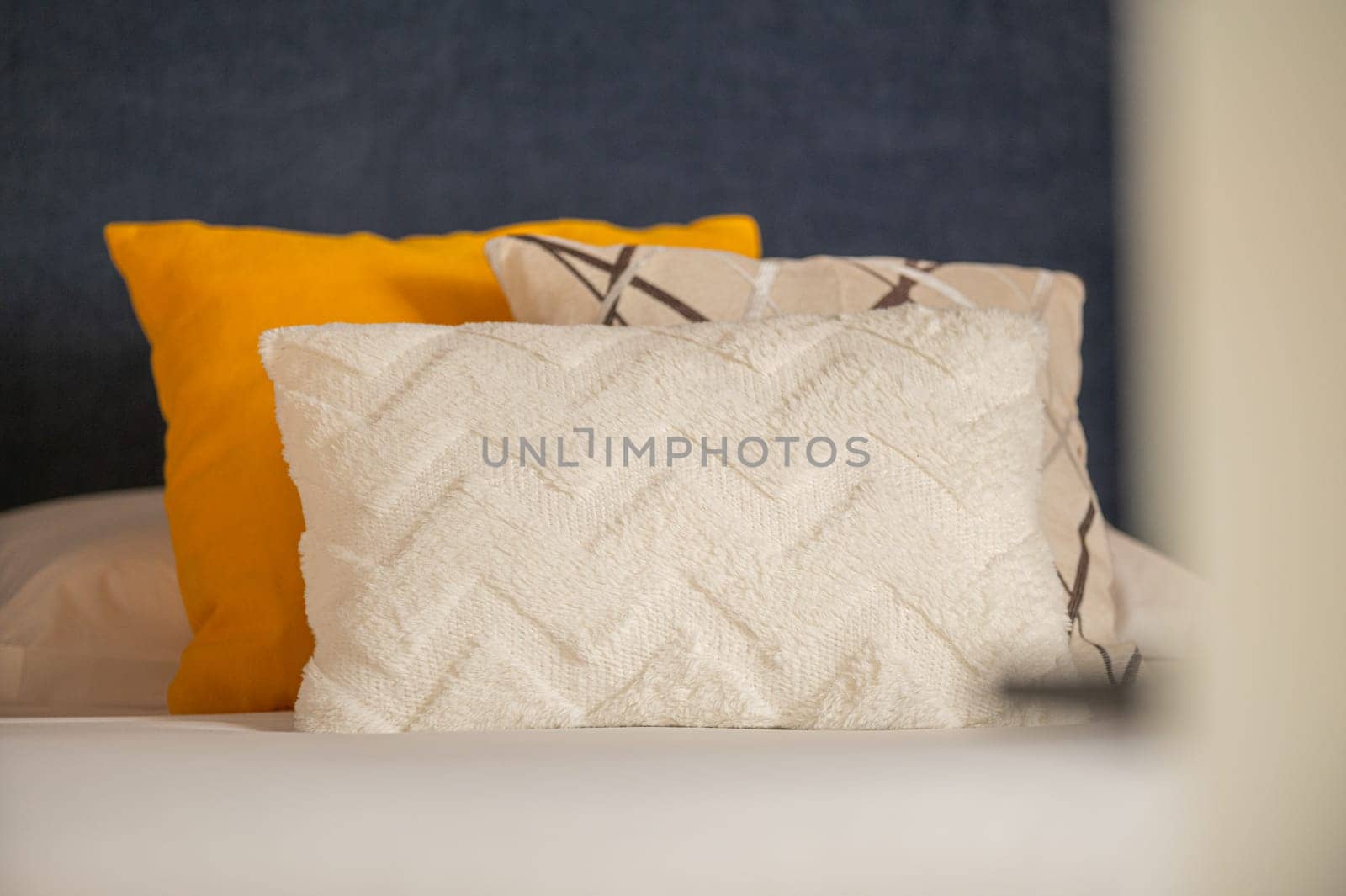 Colorful cushions on bed in illuminated room. by martinscphoto