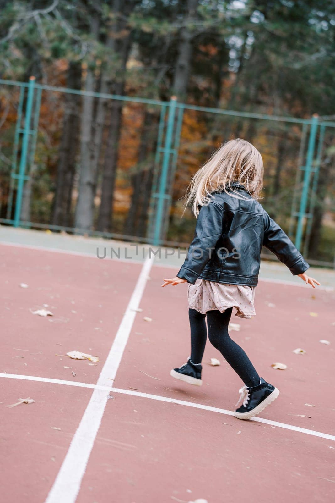 Little girl is skipping along the playground, looking to the side. Back view. High quality photo