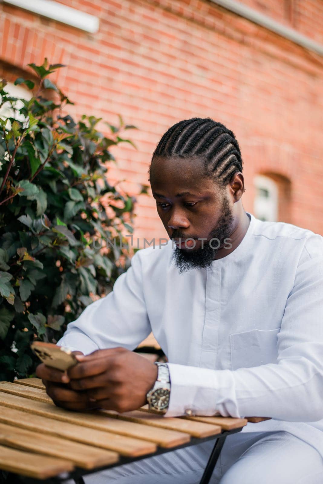 African American hipster guy in cultural and ethnic clothing dashiki chatting on smartphone outdoors, texting with friends on social networks. Millennial and Internet concept.