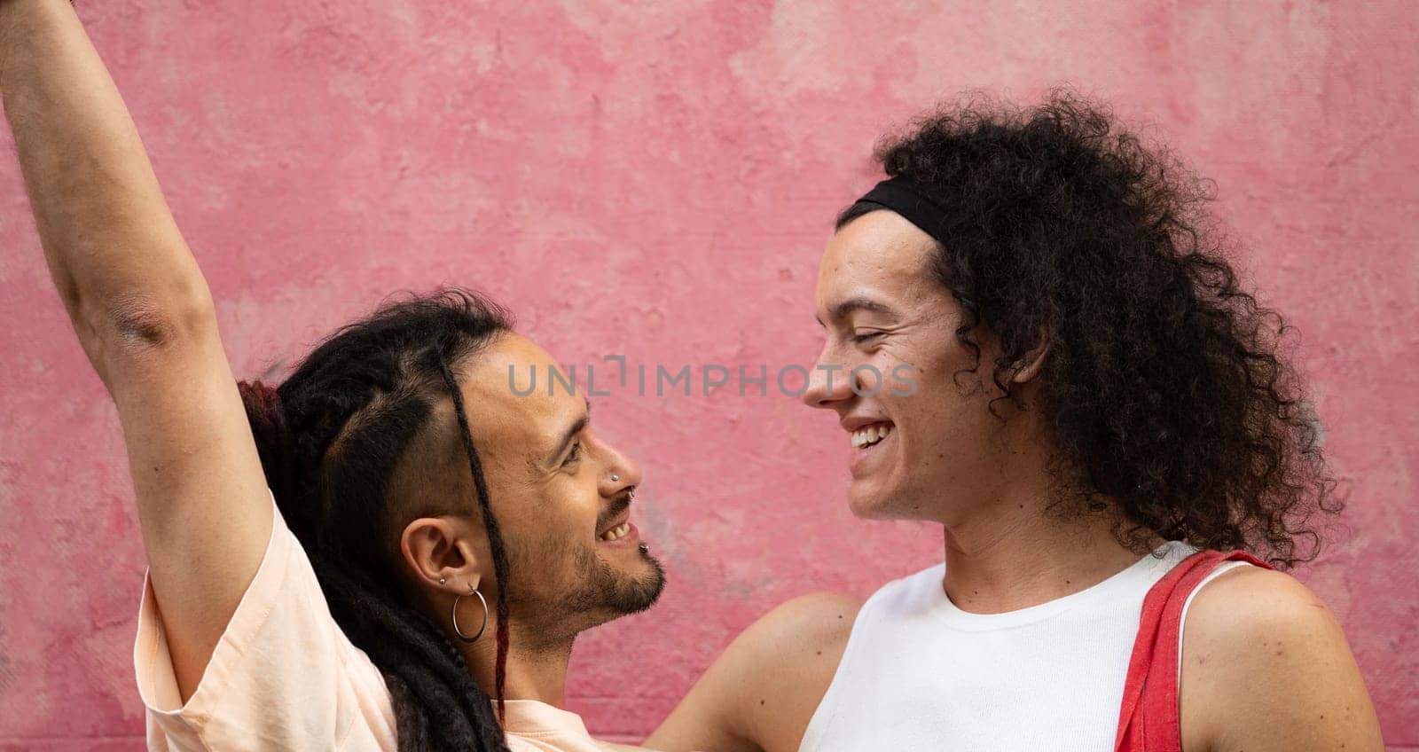 Two gay couple men are smiling and looking at each other with love and happiness isolated on pink background by papatonic