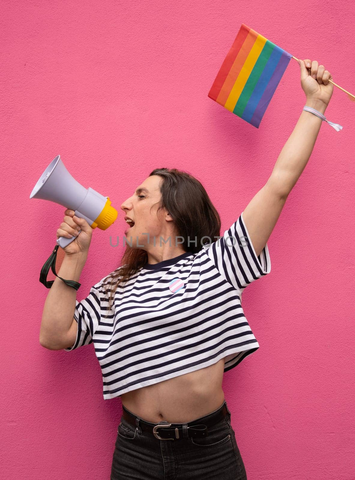 Portrait of transgender woman shouting with a megaphone and holding a rainbow flag supporting LGBTQ community.