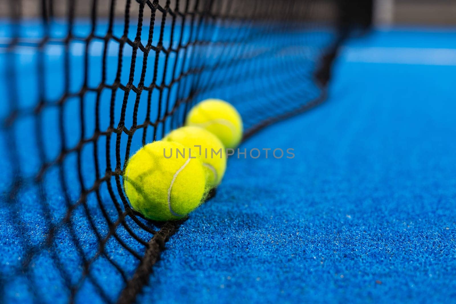 several balls by the net on a blue paddle tennis court. High quality photo