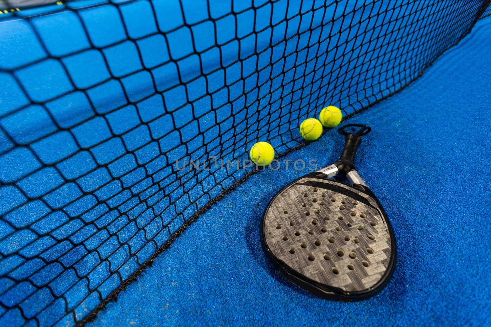 Black professional paddle tennis racket and ball with natural lighting on blue background. Horizontal sport theme poster, greeting cards, headers, website and app. High quality photo