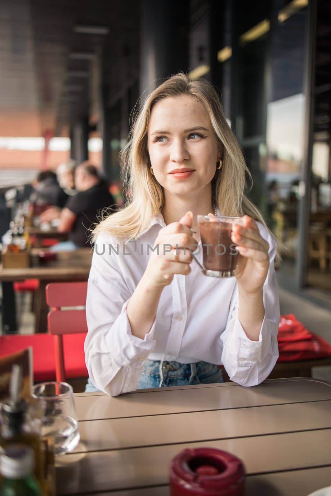 Gen z blonde woman drinks hot chocolate in summer cafe. Tasty beverage and break